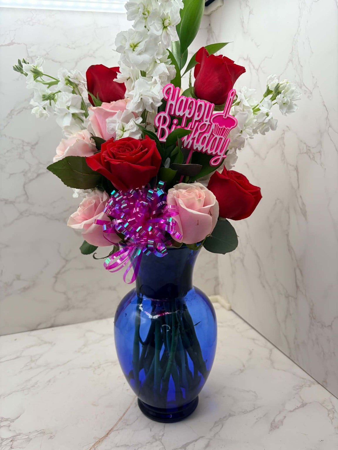 Rose Runners birthday arrangement with pink roses, white chrysanthemums, purple balloons and Happy Birthday topper