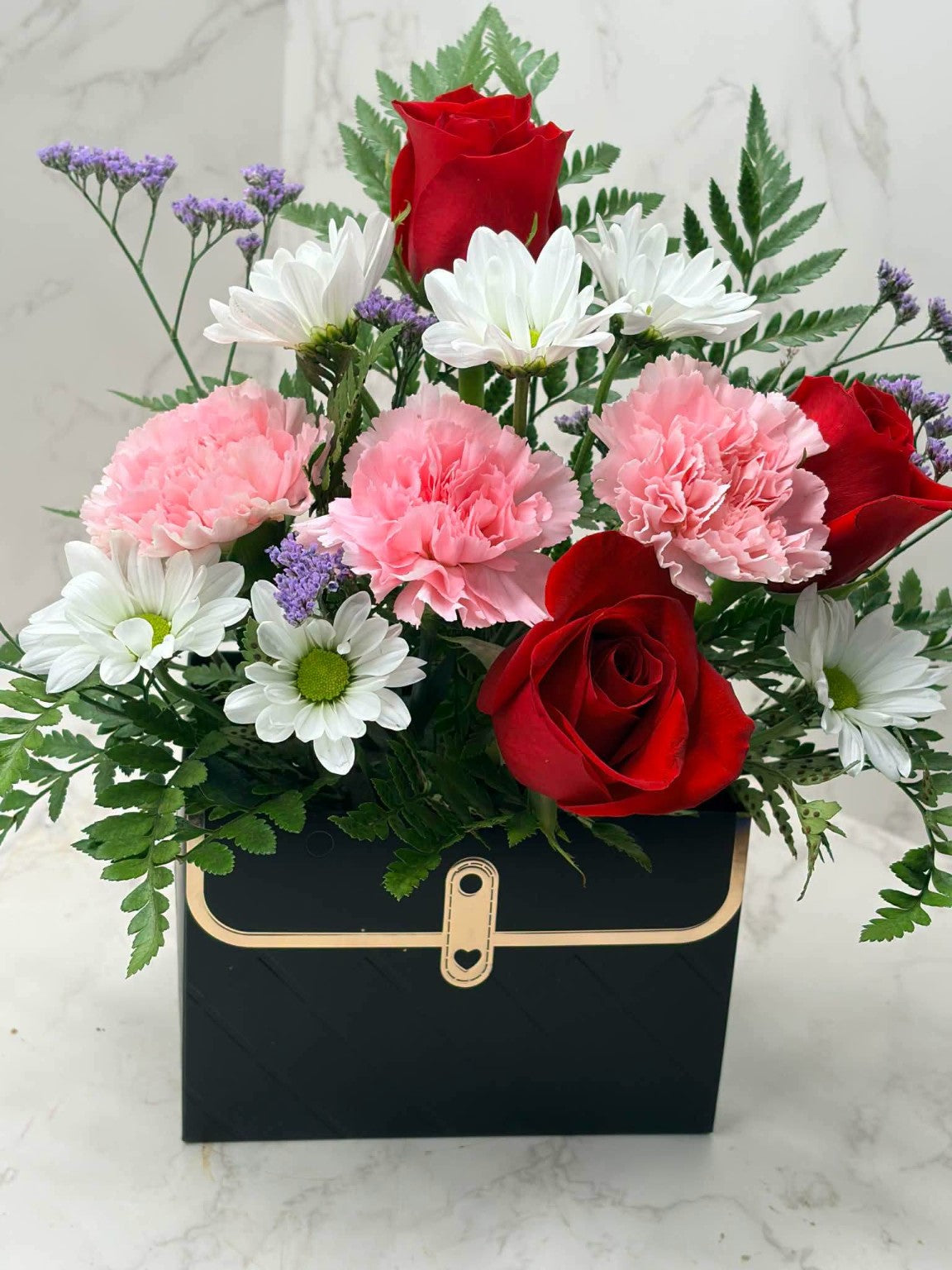 Rose Runners floral arrangement with red roses, pink carnations, white chrysanthemums and purple accents in a black decorative container