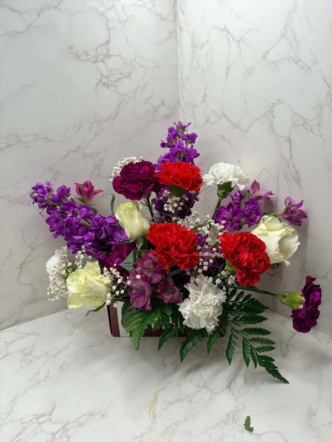 Rose Runners colorful arrangement of purple stock, red carnations and white roses in a rectangular container